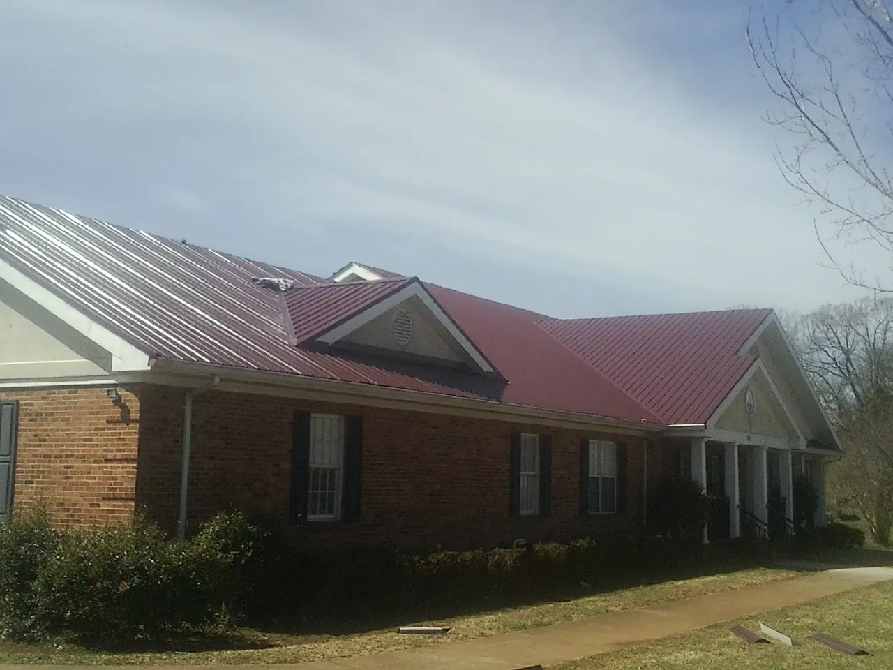 Red metal roof with gabled entries on a long brick building, from a Hail Damage Roof Repair job in Branford
