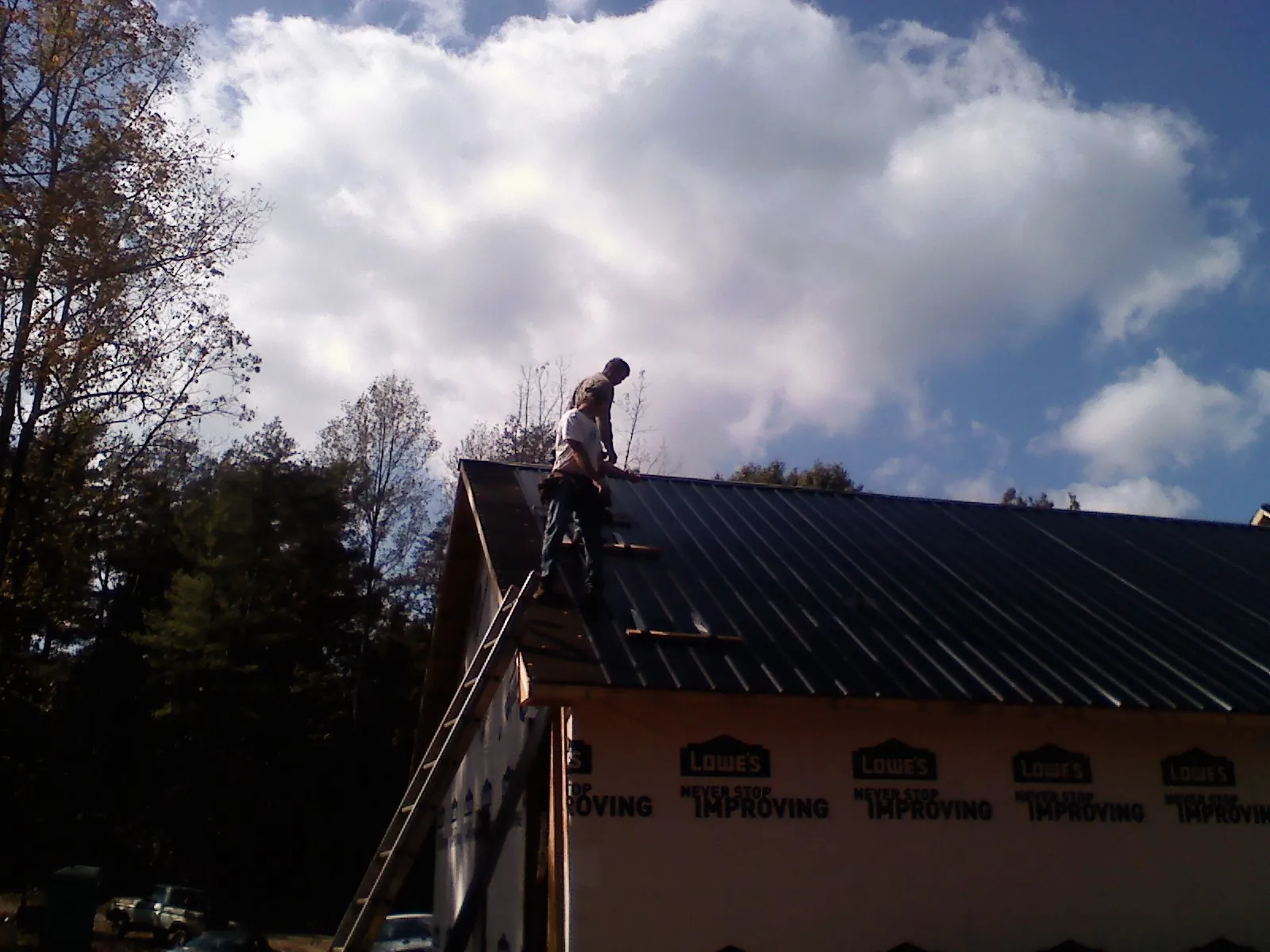 Roofer fastening dark metal panels high against a cloudy sky, from a Roof Inspection job in Branford