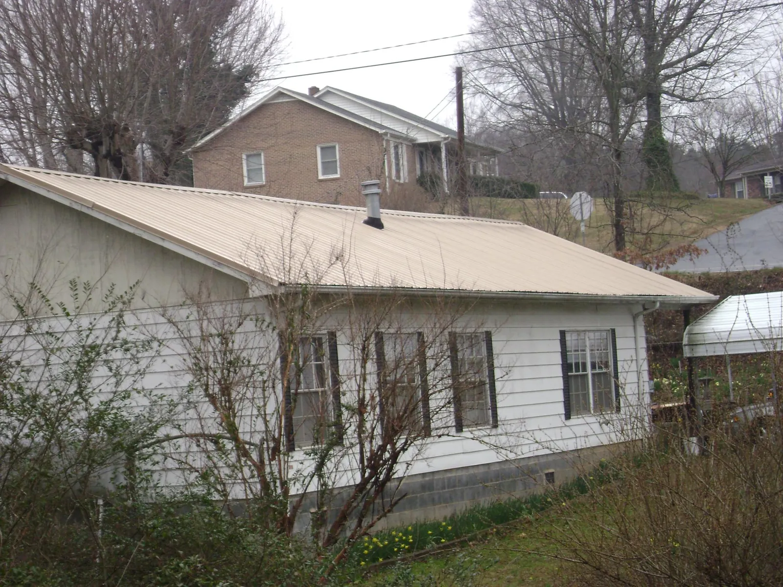 Tan metal roof on a white sided house set into a hillside — Commercial Roofing by Roofing Brothers in Branford